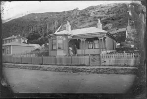 Unidentified man and woman with baby, standing on the verandah of a single-storied wooden house, Wellington
