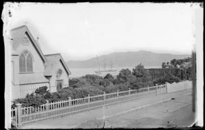 Mulgrave Street, Thorndon, Wellington, showing part of St Paul's Anglican church and a building under construction, ship in Wellington Harbour in background