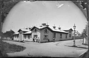 A wooden building on Museum Street, Wellington, with unidentified persons standing alongside