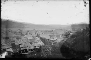 View across cottage roofs towards Wellington Harbour, showing railway yards and ships docked at wharves in distance