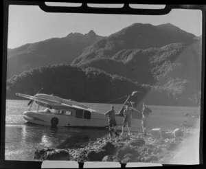 A group of unidentified men standing alongside an Amphibian Airways aircraft at George Sound, Fiordland National Park, Southland