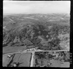 Albany, North Shore, Auckland, showing service station and [hotel or public bar] at T-intersection of two roads, tree covered hills beyond with view to the coast
