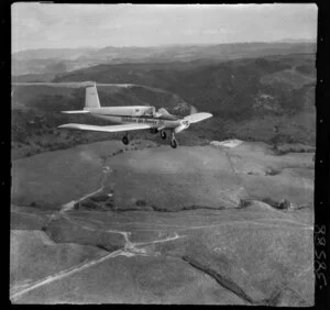 Te Kuiti, Waikato, a close-up of a Robertson Air Service Ltd aeroplane flying over hilly farmland