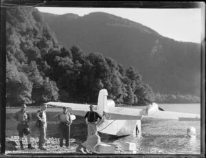 Amphibian Airways, George Sound, Fiordland, view of hunters on rocky shore with provisions, flying boat behind, with fiord beyond