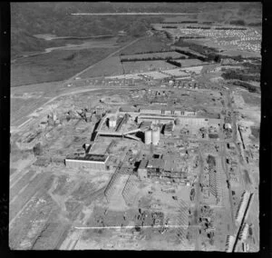 Kawerau, Bay of Plenty, showing a close-up view of Tasman Pulp and Paper Mill under construction, with new housing estate and Lake Pupuwharau beyond