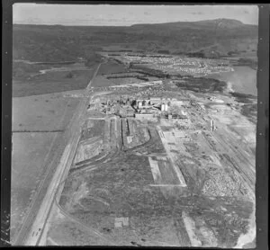Kawerau, Bay of Plenty, showing Tasman Pulp and Paper Mill under construction with Tamarangi Drive (State Highway 34) to housing development and Lake Pupuwharau beyond