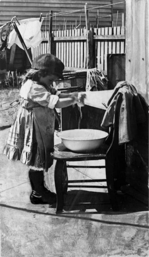 A young child washing doll's clothes in a basin