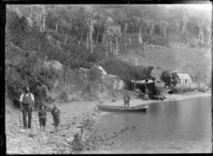 Beach at an unidentified location, possibly Marlborough Sounds, including small wooden buildings, a dry-docked boat propped up on logs, and unidentified men and boys on the shore