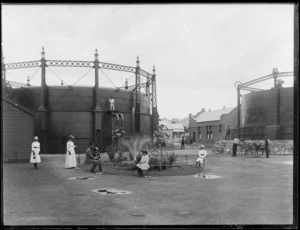 Unidentified women, man and children beside a small fountain and garden at the Napier Gas Company