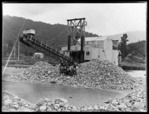 Group of directors with boy seated on pile of rocks in front of the Argo dredge