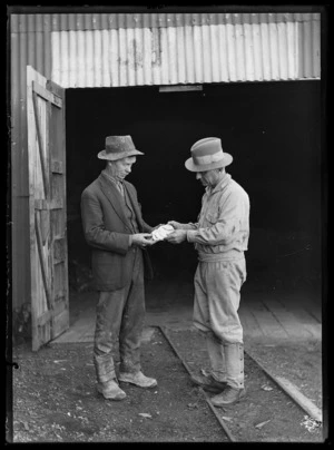 Portrait of Jack Lake (manager of Big River mine) showing a piece of quartz to Joseph Divis, in front of boiler house lean-to