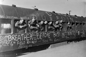 Soldiers, leaning out of a train which is covered in graffiti, as they depart to serve in World War II