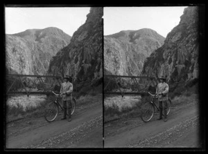 Joseph Divis holding bicycle on road next to Karangahake River, with rail bridge in background