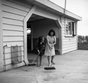 Two girls sweeping the rubbish from outside a school building at Te Kaha