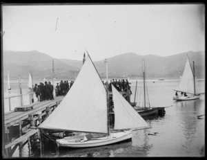 Crowd standing on jetty at Broad Bay, Dunedin, with a small sailing boat in the foreground