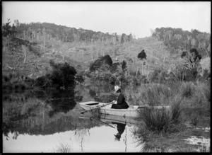 Woman [Lydia Myrtle Williams?] reading in boat resting in rushes, Owaka River, Clutha District, Otago Region
