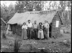Thomas H Wyatt (far right), Jack Byrne (2nd left) and unidentified Maori man and women beside a thatched whare, Te Kauri, Otorohanga County