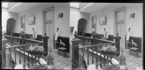 Interior of Crescent Hotel, Invercargil, Southland Region, featuring stuffed penguins, mounted albatross head, another unidentified bird, and an elderly lady [Mrs R Bond?] leaning on the balustrade