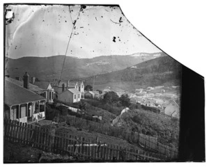 View of hilly built-up area on ridge above the port at Port Chalmers, looking towards Sawyers Bay from Scotia Street, with snow-covered Mount Cargill at rear, ca 1870s.