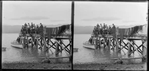 A group of well-dressed men and women sitting on a wharf, with fishing nets draped alongside, Akaroa, Banks Peninsula