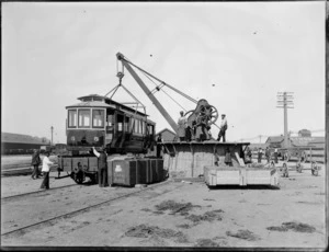 Men using a crane to load a tram for Whanganui onto a train carriage, Christchurch railyards
