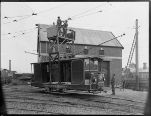 Men in a Christchurch Tramways vehicle, repairing overhead tram wires , including tram shed in background