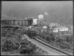 A Westport Coal Company steam locomotive hauling coal through a settlement which includes workshops and houses, location unidentified