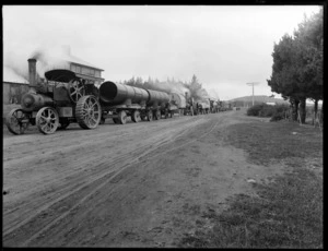 Convoy of steam traction engines towing wagons, on a rural road, possibly Canterbury region
