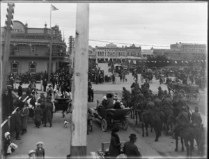 Spectators and mounted regiment at War World I parade, The Square, Palmerston North, including hotel on corner of Main Street West, and business premises of Kew Kong Fruiterer, Gilchrist and Kido land agents, and AE Clausen