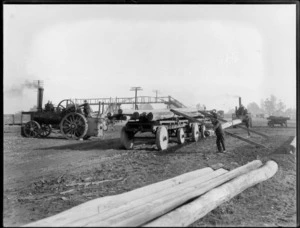 Men using a steam traction engine to pull [telegraph?] poles onto a wagon, showing a steel bridge in background, Sockburn, Christchurch