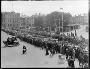 Crowd of people on Christchurch City street, welcoming home invalided soldiers transported within cars, also trams and Reuters Telegram Company building