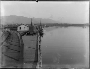 [Buller Company?] building and wharf area, with crane and tugboat, railway track with coal wagons and station behind, Westport Harbour