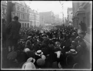 Crowd welcoming home World War I invalided troops with street parade, showing cars with troops and nursing staff, crowd filling street and any vantage point they can, beside Wellington Town Hall and commercial buildings Office Appliance Co and Smith & Smith with flags