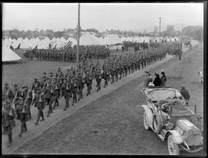 World War I soldiers marching down road of training camp, with senior officer and women beside a car looking on, other soldiers lining up beside tents beyond, [possibly Burnham Military Camp, Christchurch?]