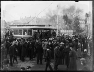 View of a Tramways tram with people boarding and milling around, safety device on front, Christchurch City