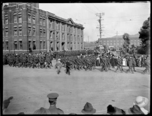 World War I soldiers on parade [Wellington ?] with crowds of people looking on, in front of large brick building, with dock area warehouses beyond