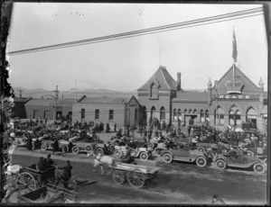 Peace celebrations outside Christchurch Railway Station after World War I with line of motor cars, and crowd including sailors