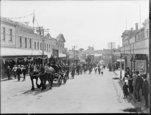 Timaru Voluntary Fire Brigade parade, showing horse-drawn floats on a street lined with commercial buildings, Timaru, to celebrate the coronation of George V