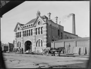 Christchurch Municipal Baths building, with two horses and carts out the front, a man tending to one of the horses and the other man cleaning the pathway