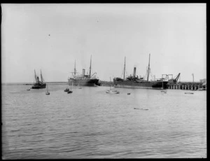 Two ships docked at the wharf, Timaru, with a tugboat and small boats in the foreground