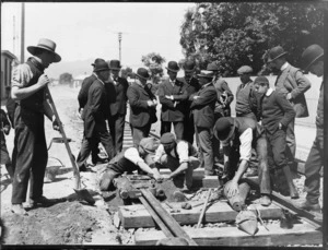 'Thermit welding device' on street tram rails, showing workmen operating the device with dignitaries looking on, Canterbury region