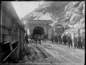 Group at entrance of the Otira Tunnel, Westland, including the Union Jack flying above and a man with a camera