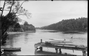 Unidentified man in a boat with the Union Flag flying at stern, including a wharf, [Fiordland National Park, Southland District?]