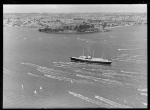 The Royal Yacht HMY Britannia, arriving in Auckland, showing the ship sailing in Waitemata Harbour, with a flotilla of small yachts