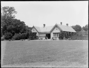 A large wooden house with a large lawn and an unidentified man and woman on front steps, Christchurch