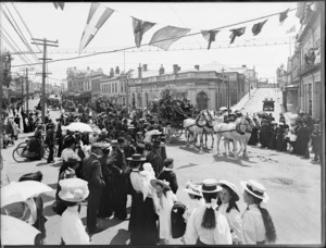 Crowds gather to watch the parade, led by a horse-drawn carriage on a street lined with commercial buildings, Timaru, to celebrate the coronation of George V