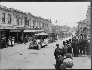 A fleet of motor cars in parade, on a street lined with commercial buildings, Timaru, to celebrate the coronation of George V