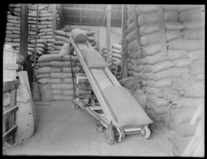 Conveyor belt moving sacks at the business of S Wright & Company, Addington, Christchurch, including other sacks piled up in the background