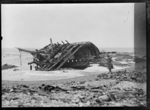 Shipwreck on an unidentified beach, including an unidentified person in rain coat and hat, holding a gun, possibly Christchurch