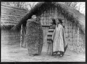 [South Seas Exhibition?], at the marae exhibit, two Maori women dressed in cloaks, with a pakeha man holding a Maori child dressed in a cloak